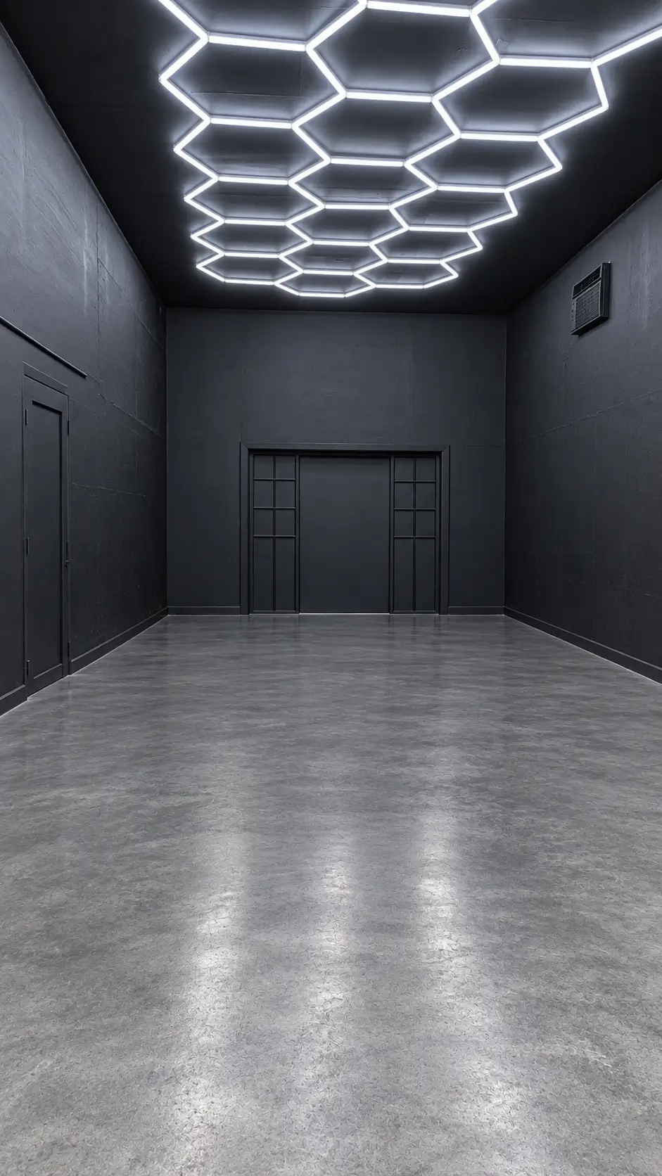 Empty storage and service area of the West section at 830 NE 79th St, Miami, with polished concrete floors, dark walls, hexagonal LED ceiling lighting and a wide door.