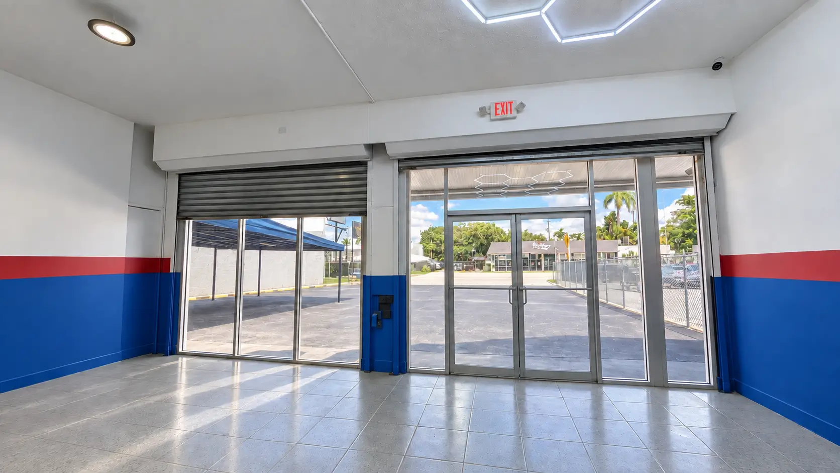 View from inside the showroom through the glass entrance and roll-up door to the fenced front lot.