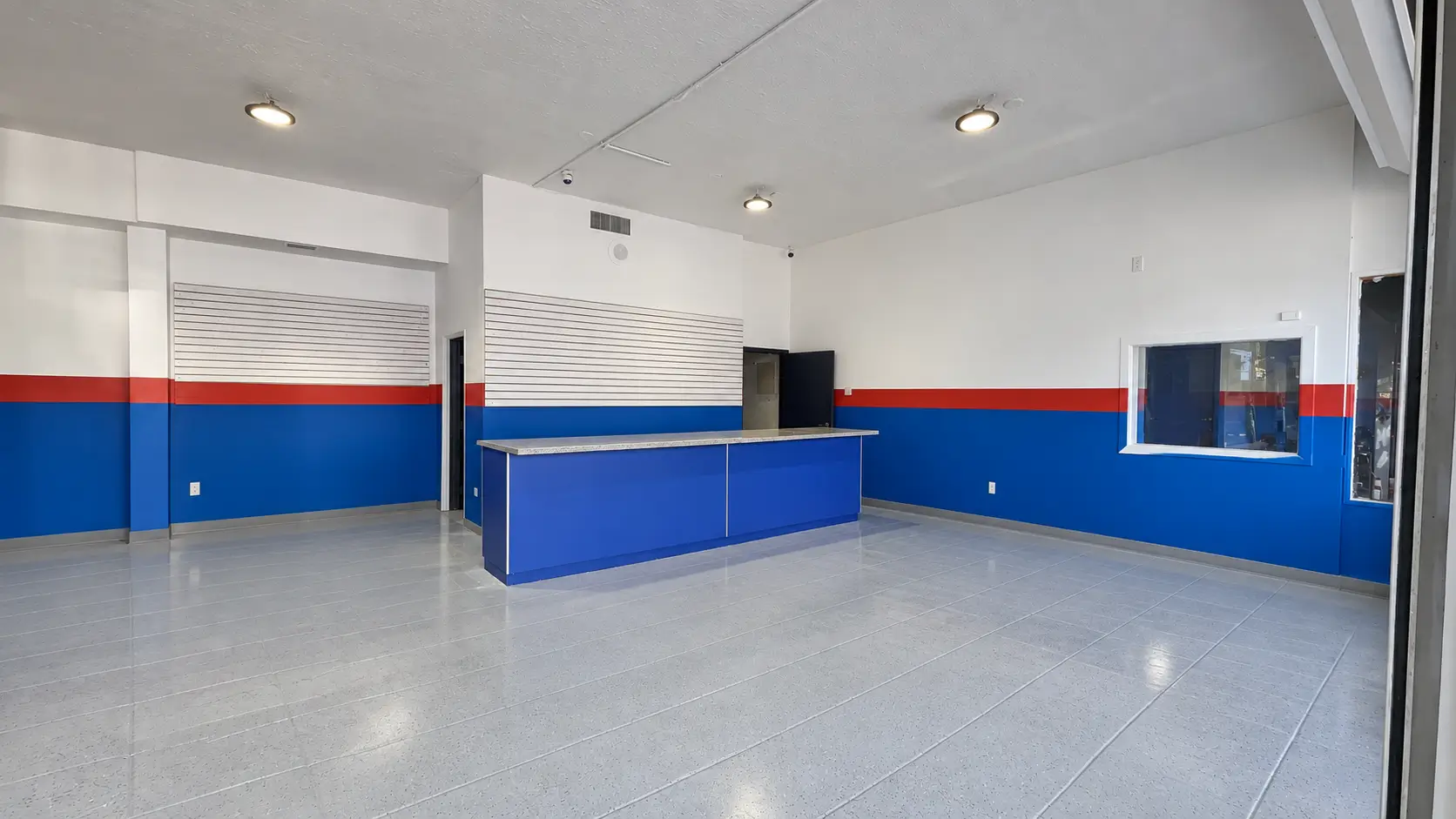 Empty showroom of the West section at 830 NE 79th St with a blue service counter, slatwall displays and polished floors.